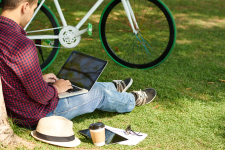 Man with laptop sitting on grass in city parkの写真素材