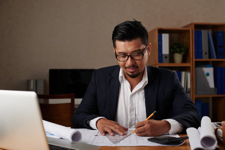 Architect working with blueprint at his tableの写真素材