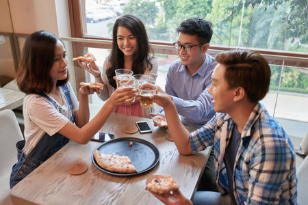 Vietnamese friends enjoying pizza and drinks in cafeの写真素材