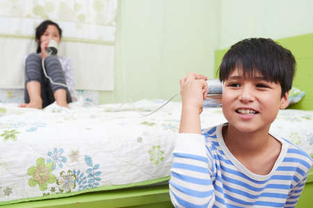 Brother and sister playing with tin can telephoneの写真素材