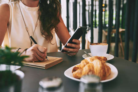 Female hands writing information in notebook from phoneの写真素材