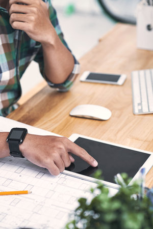 Designer using digital tablet while working with on blueprint