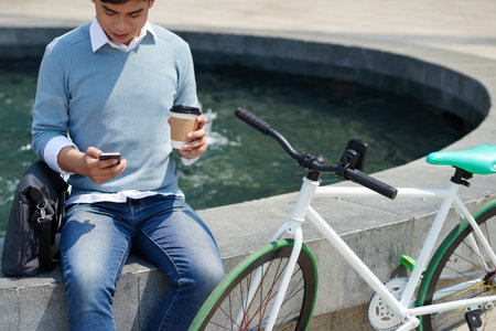 Cropped image of guy using application on his phone when resting outdoors