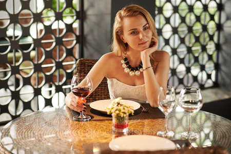 Gorgeous young woman drinking red wine alone in restaurantの写真素材