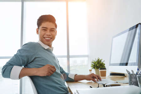 Portrait of cheerful Asian businessman at his workplaceの写真素材