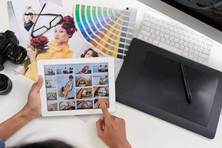 Editor looking through photos on digital tablet, view from aboveの写真素材