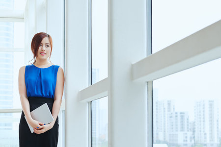 Lovely young business lady looking through office windowの写真素材