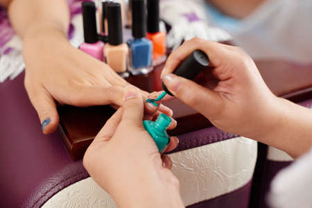 Close-up image of manicurist painting nails greenの写真素材