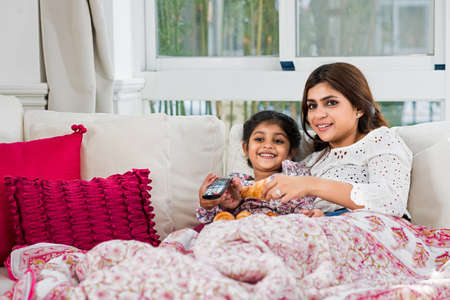 Indian mother and daughter lying on sofa and watching tvの写真素材