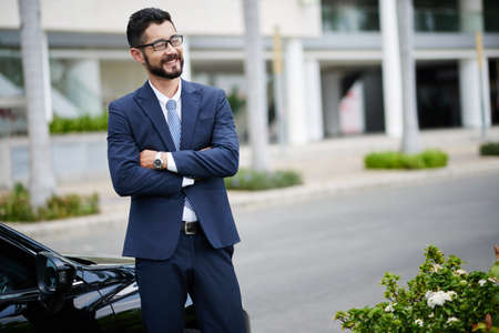 Happy entrepreneur standing at car with his arms foldedの写真素材