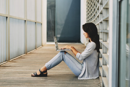 Side-view of woman sitting on floor and working on laptopの写真素材