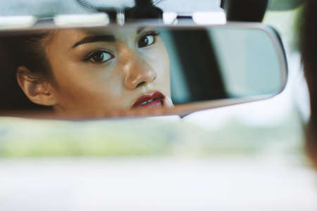 Reflection of attractive woman looking at car mirrorの写真素材