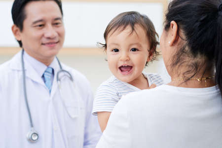 Cute baby boy laughing when his mother talking to doctorの写真素材