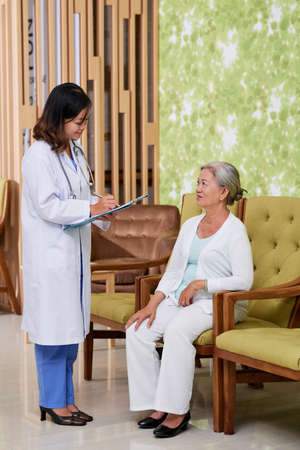 Nurse writing down complains of senior womanの写真素材