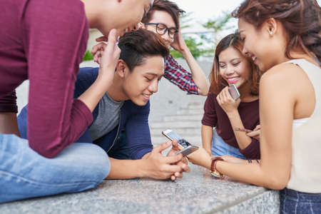 Group of Vietnamese young people gathered at smartphone of friendの写真素材