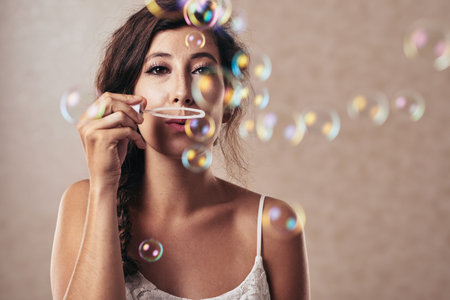 Pretty brunette blowing soap bubbles and looking at camera
