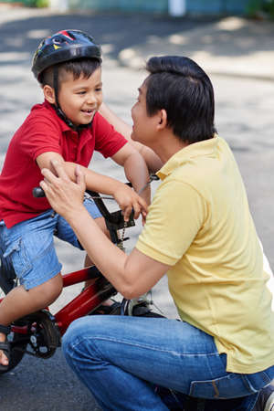 Father supporting his little son before cyclingの写真素材