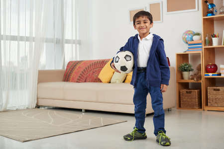 Portrait of cheerful little boy with soccer ball standing at homeの写真素材