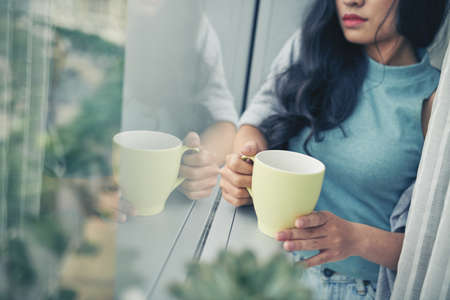 Cropped image of woman with cup of coffee standing at windowの写真素材