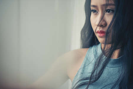 Portrait of pensive unsmiling Vietnamese woman at windowの写真素材
