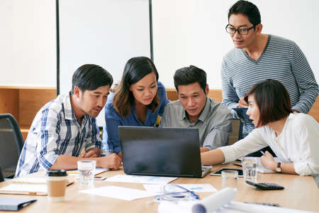 Asian business team discussing information on laptop screenの写真素材