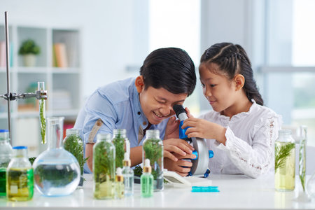 Curious Asian boy and girl using microscope in classの写真素材