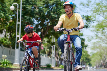 Vietnamese father and son in helmets cycling in the cityの写真素材