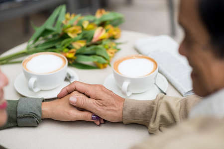 Senior man touching hand of his wife when they sitting in cafeの写真素材