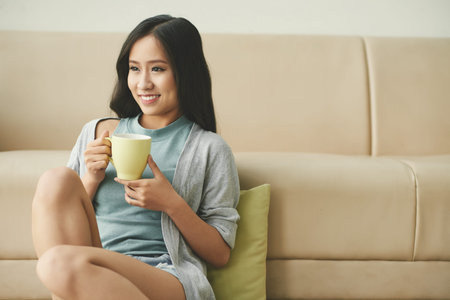 Smiling attractive girl sitting on the floor and drinking tea