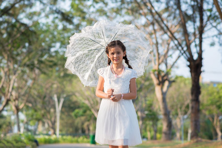 Cute young woman with lace umbrella standing in parkの写真素材
