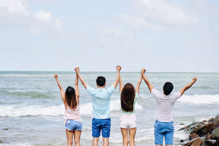Rear view of young people standing at the beach and holding handsの写真素材