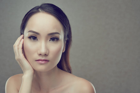 Portrait of unsmiling Asian woman, isolated on grey