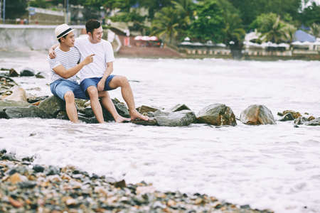 Happy Vietnamese gay couple sitting on rocksの写真素材