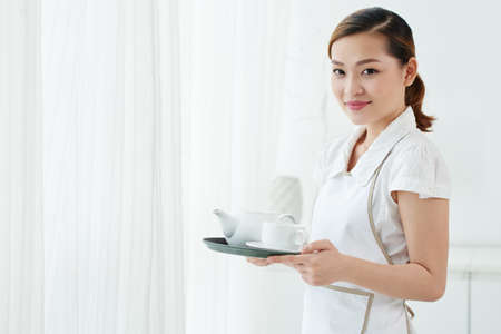 Chambermaid holding teapot and cup on a trayの写真素材