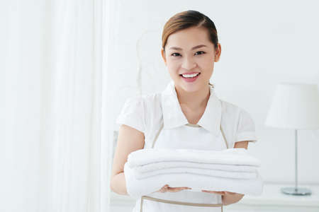 Beautiful smiling chambermaid changing towels in hotel roomの写真素材