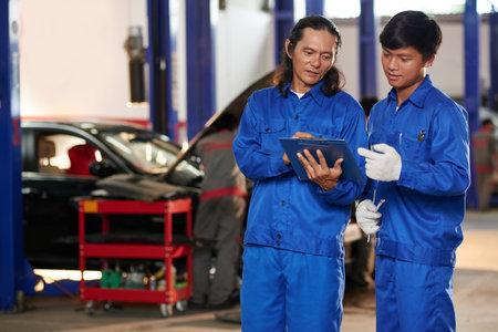 Professional Asian mechanics discussing car fixing in garageの写真素材