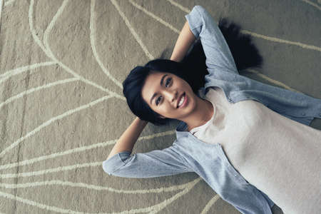 Cheerful mixed-race girl lying on floor and looking in cameraの写真素材