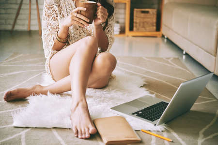 Woman enjoying mug of coffee when sitting on floorの写真素材