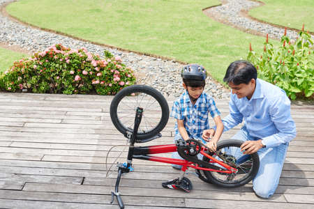 Indian man showing his son how to repair bicycleの写真素材