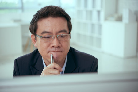 Pensive Asian businessman looking at computer screenの写真素材