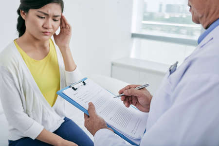 Young woman complaining about headache to her doctorの写真素材