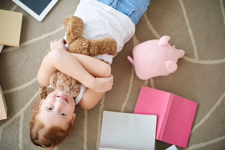 Joyful girl hugging teddy bear when lying on floorの写真素材