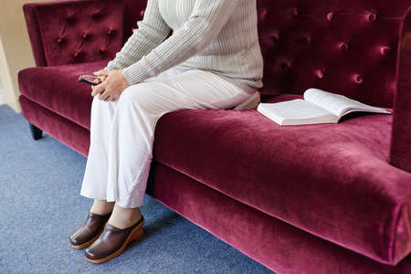 Legs of aged woman sitting on sofa aloneの写真素材