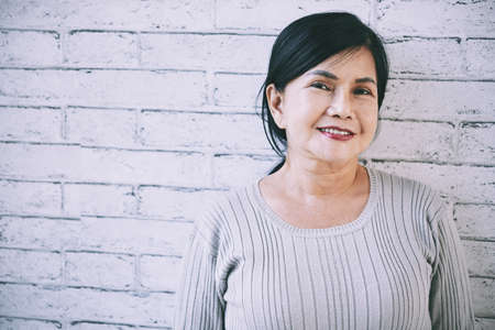 Senior Vietnamese woman standing at brick wallの写真素材