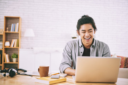 Portrait of cheerful young man working on laptop at home