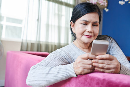 Pretty senior woman sitting on sofa and text messaging