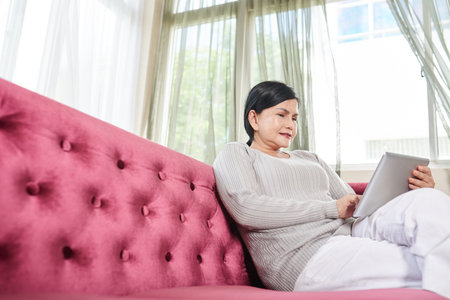 Senior woman relaxing on sofa with tablet computerの写真素材