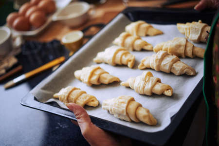 Woman putting tray of croissants in hot ovenの写真素材