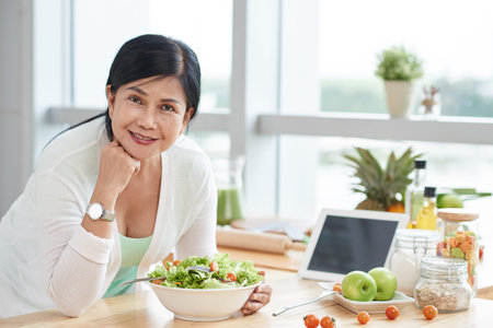Cheerful Asian woman eating salad at homeの写真素材
