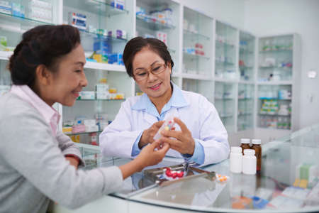 Senior Vietnamese pharmacist and customer discussing medicationsの写真素材